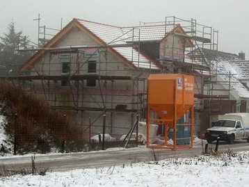 Rohbau eines Einfamilienhauses im Winter mit Schnee auf der Baustelle und sichtbarem Mauerwerk.
